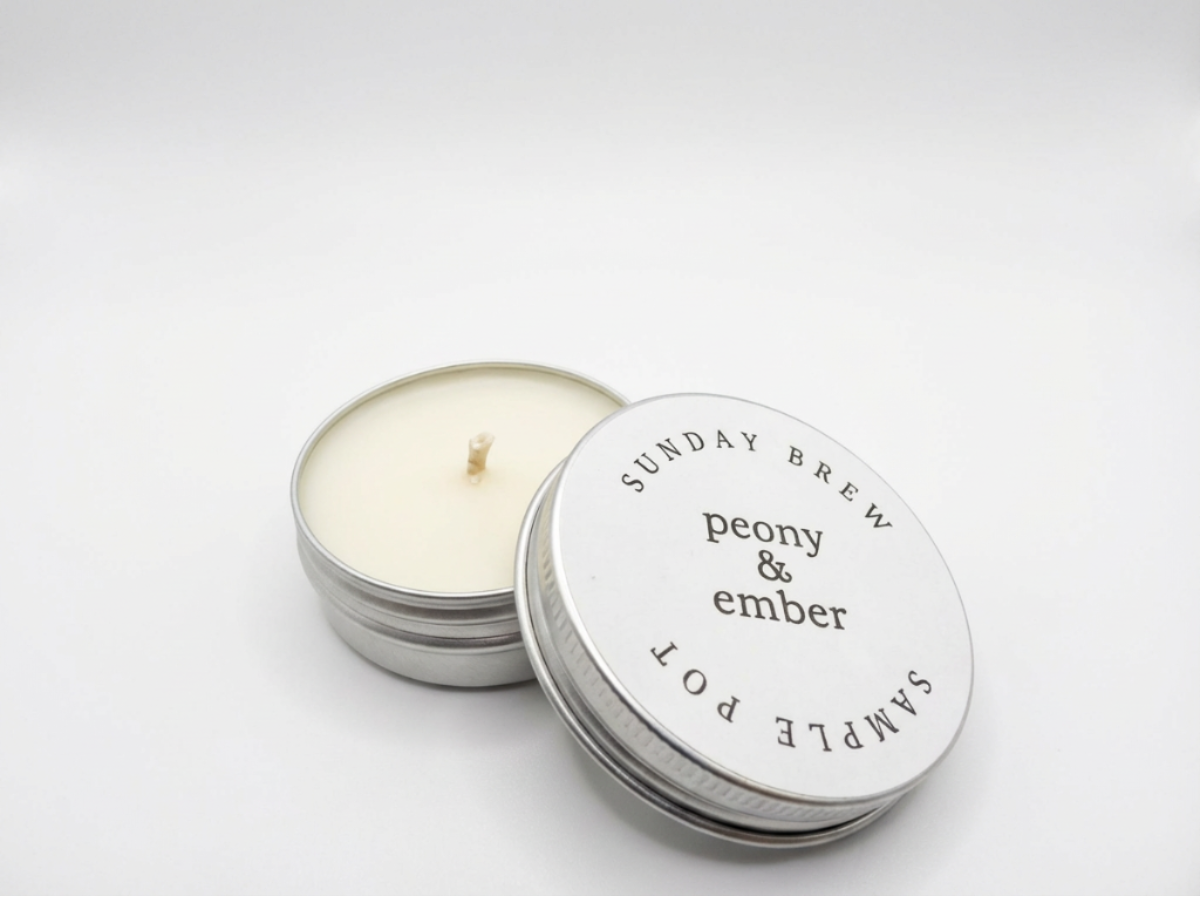 Candle sample in a tin labelled 'Sunday Brew' with the brand name 'Peony & Ember' in the middle on a white background