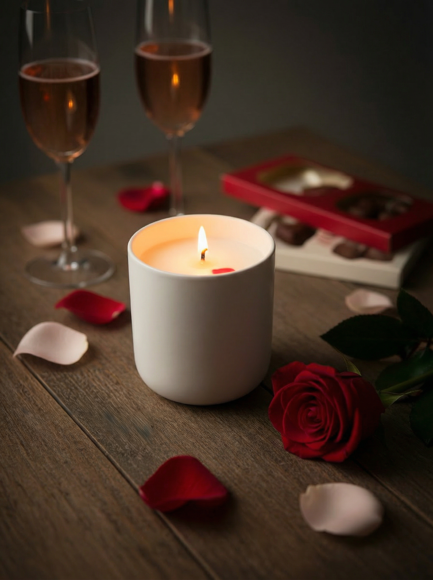 Lit Peony & Ember Valentine’s Day candle in a white ceramic jar, photographed with rose petals, a red rose, chocolates, and sparkling rosé glasses to create a romantic luxury home fragrance setting